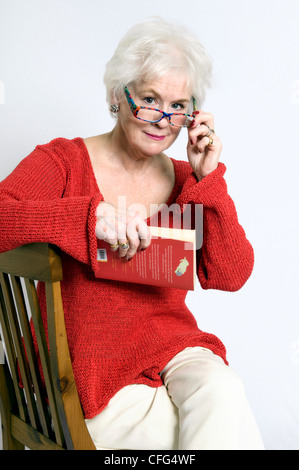 Attractive senior lady holding a book in one hand and holding out reading glasses in another Stock Photo