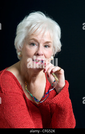 Attractive senior lady holding reading glasses in corner of mouth Stock Photo