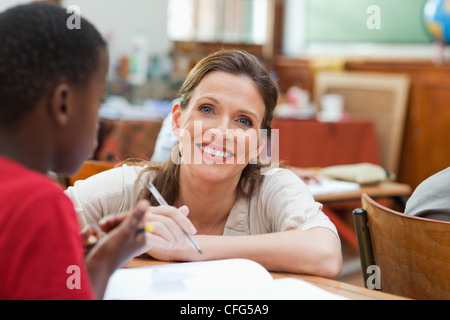 Smiling teacher kneeling next to students desk Stock Photo - Alamy
