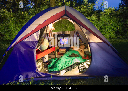 A young man sleeps in his tent surrounded by electronic gear and other camping equipment. Stock Photo