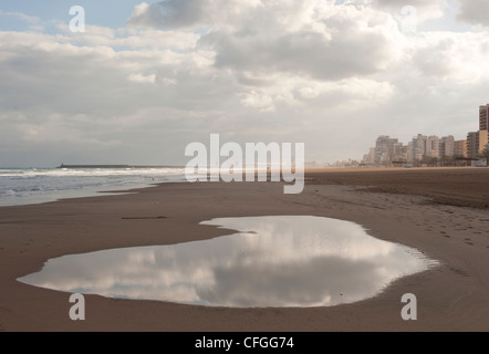 A large puddle reflects a stormy cloudy sky above the sea as rain sets in during winter on the Spanish resort of Gandia, Spain Stock Photo