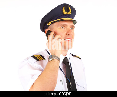 Cheerful pilot wearing uniform with epaulets and hat with golden wings, talking on mobile phone, standing isolated on white Stock Photo