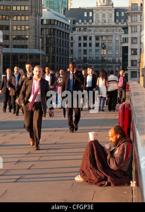 Commuters walking across London Bridge in City of London financial district England UK with homeless man in foreground Stock Photo