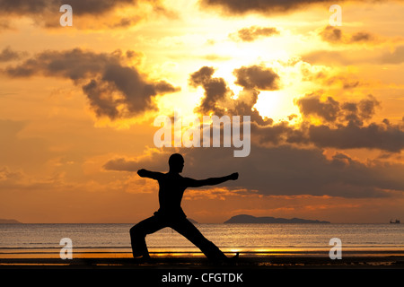 Man silhouette doing yoga exercise archer at sunset beach Stock Photo
