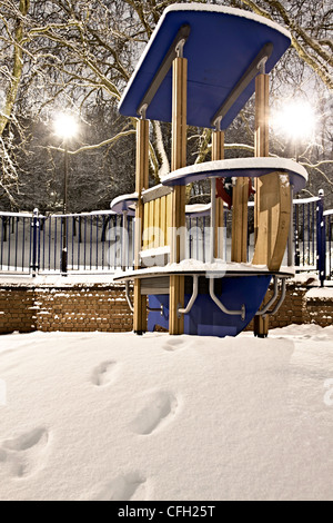 Toy playground boat for children photographed at night in the snow with footsteps leading to it Stock Photo