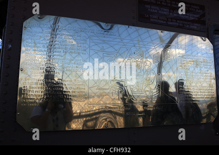 Reflections of people visiting the Eiffel Tower on a brass plaque outside a replica office of Gustave Eiffel's Stock Photo