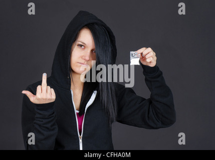 Young woman drug addict or dealer showing a packet of drugs and givng the viewer the finger. Stock Photo