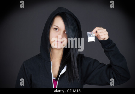 Gloomy portrait of a young woman or teen addict looking sad showing her little bag of drugs. Stock Photo