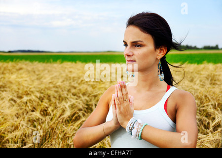 Beatiful and healthy natural young woman embracing nature by doing meditation, yoga or tai chi in a riped wheat field. Stock Photo