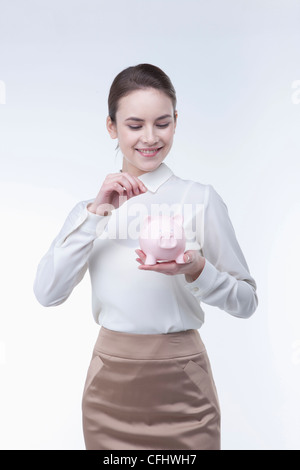 Businesswoman putting a coin into a piggy bank Stock Photo - Alamy
