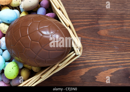 Still life photo of a large chocolate easter egg in a basket surrounded by candy covered mini eggs Stock Photo