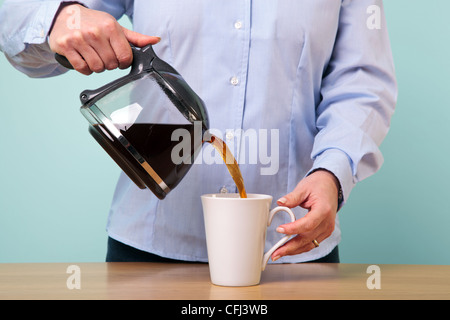 Photo of a woman on her break pouring herself a mug of hot filtered coffee from a glass pot. Stock Photo