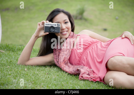 Young woman lying on grass and taking photo with camera Stock Photo