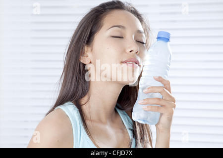Young woman putting plastic bottle on cheek Stock Photo