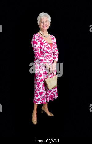 Full length shot of attractive senior lady in pink dress holding handbag taken against a black background Stock Photo