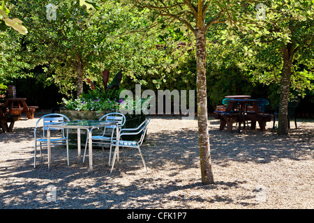 Cafe tables in dappled shade of  trees on gravel patio in English country garden of Littlecote Manor in Berkshire, England, UK Stock Photo