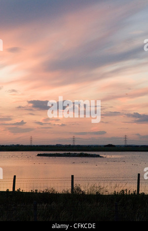 Sunset image with silhouette of fence and pylons over water. Stock Photo