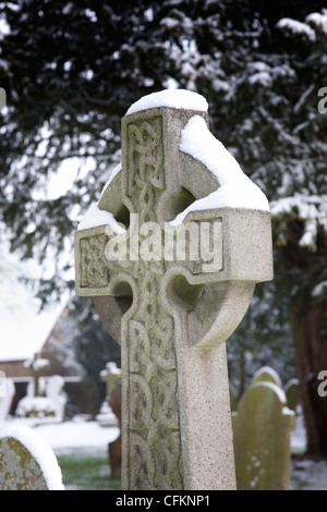 Snow lying on a headstone with a celtic pattern, in a churchyard. Stock Photo