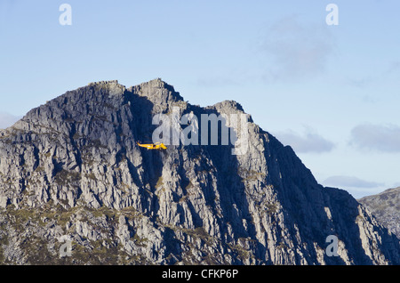 Yellow RAF Seaking rescue helicopter hovering near steep crags of Mt Tryfan east face in mountains of Snowdonia North Wales UK Stock Photo