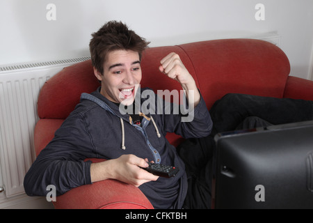 Young man watching tv alone, cheering and punching the air celebrating. Stock Photo
