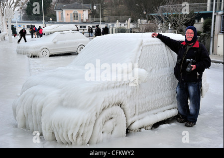 Photographer standing by a car frozen in ice in Versoix, Switzerland, by Lake Geneva Stock Photo