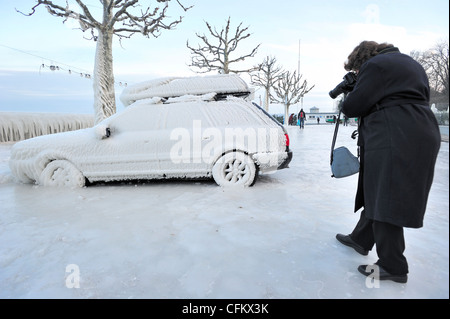 A woman taking a photograph of a car frozen in ice in Versoix, Switzerland, by Lake Geneva Stock Photo