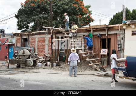 cement dust coats workmen carrying buckets fresh cement to 2nd floor of house under construction where foreman directs pouring Stock Photo