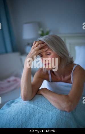 USA, New Jersey, Jersey City, Senior woman sitting in bed and suffering from headache Stock Photo