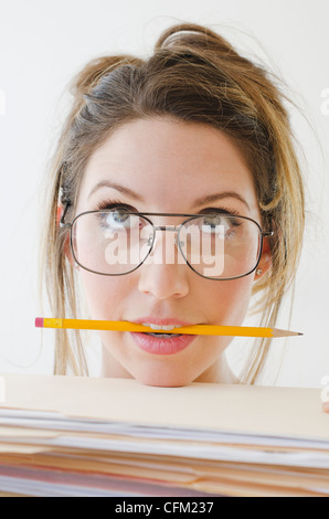 Portrait of young woman wearing glasses and holding pencil in mouth, studio shot Stock Photo