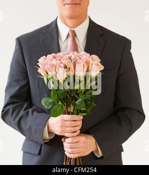 Close up of man in suit holding bouquet of roses, studio shot Stock Photo