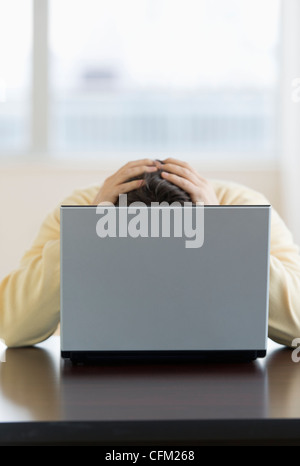 Jersey City, New Jersey, Stressed man sitting at desk behind laptop with head in hands Stock Photo