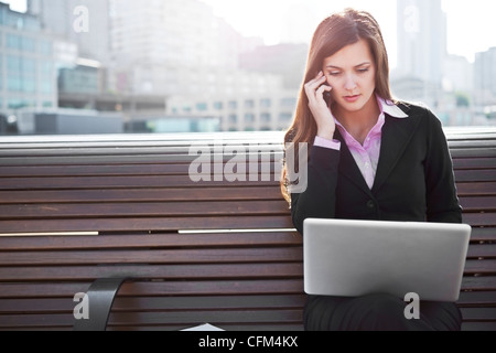 USA, Seattle, Young businesswoman sitting on bench and working Stock Photo