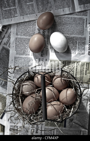 Eggs in a basket with straw on newsprint Stock Photo
