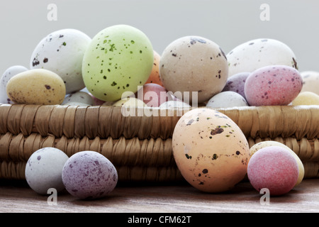 Still life photo of speckled candy covered chocolate easter eggs in a wicker basket on a rustic wooden table. Stock Photo