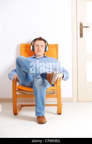 Man with closed eyes listening music with headphones sitting on chair at home Stock Photo