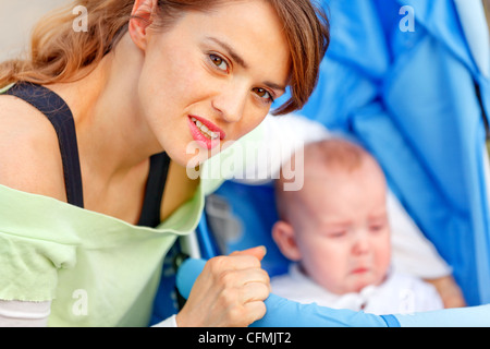 Caring young mother hugging sitting in stroller crying baby Stock Photo