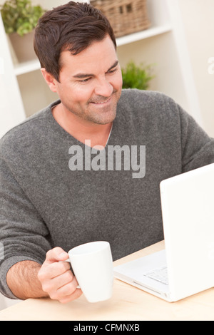 Smiling man in his thirties at home using his laptop computer drinking tea or coffee Stock Photo