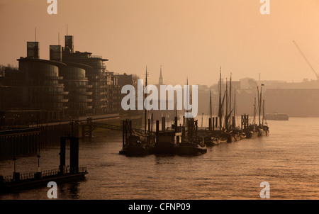 Looking along the Thames north bank from Tower Bridge sees the moored boats and river apartments emerging through London's mist