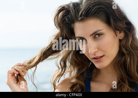 Young woman playing with ends of hair, smiling flirtatiously at camera Stock Photo