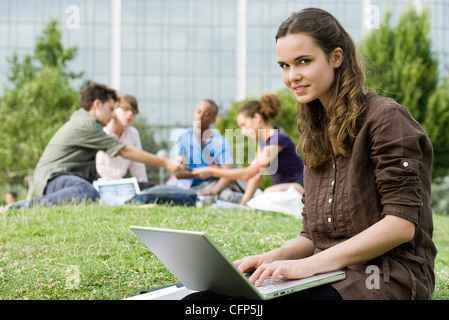 Young woman using laptop computer on grass, people in background Stock Photo