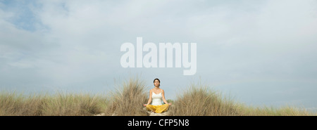 Mature woman meditating on beach Stock Photo