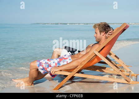 Two men sitting side by side on beach looking at ocean Stock Photo