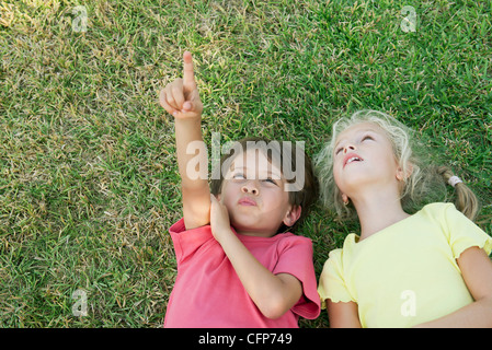 Boy and girl lying on grass, looking up and pointing Stock Photo