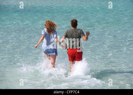Couple running into water holding hands, rear view Stock Photo