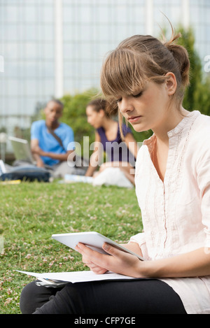 Young woman reading electronic book on grass, people in background Stock Photo