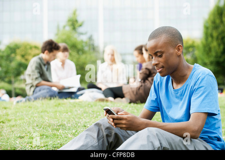 Young man text messaging with cell phone, people in background Stock Photo