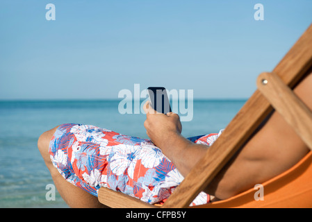 Man using cell phone while sitting on beach, cropped Stock Photo