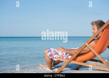 Young man reclining in deckchair looking at ocean, side view Stock Photo