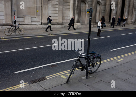 Londoners and two bicycles locked to posts on opposite sides of the road outside the Bank of England in the City of London. Stock Photo