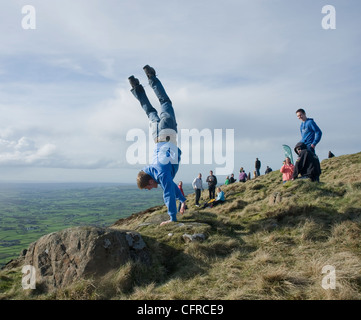 Young man doing somersault on summit of Slemish during St. Patrick's Day pilgrimage. Stock Photo